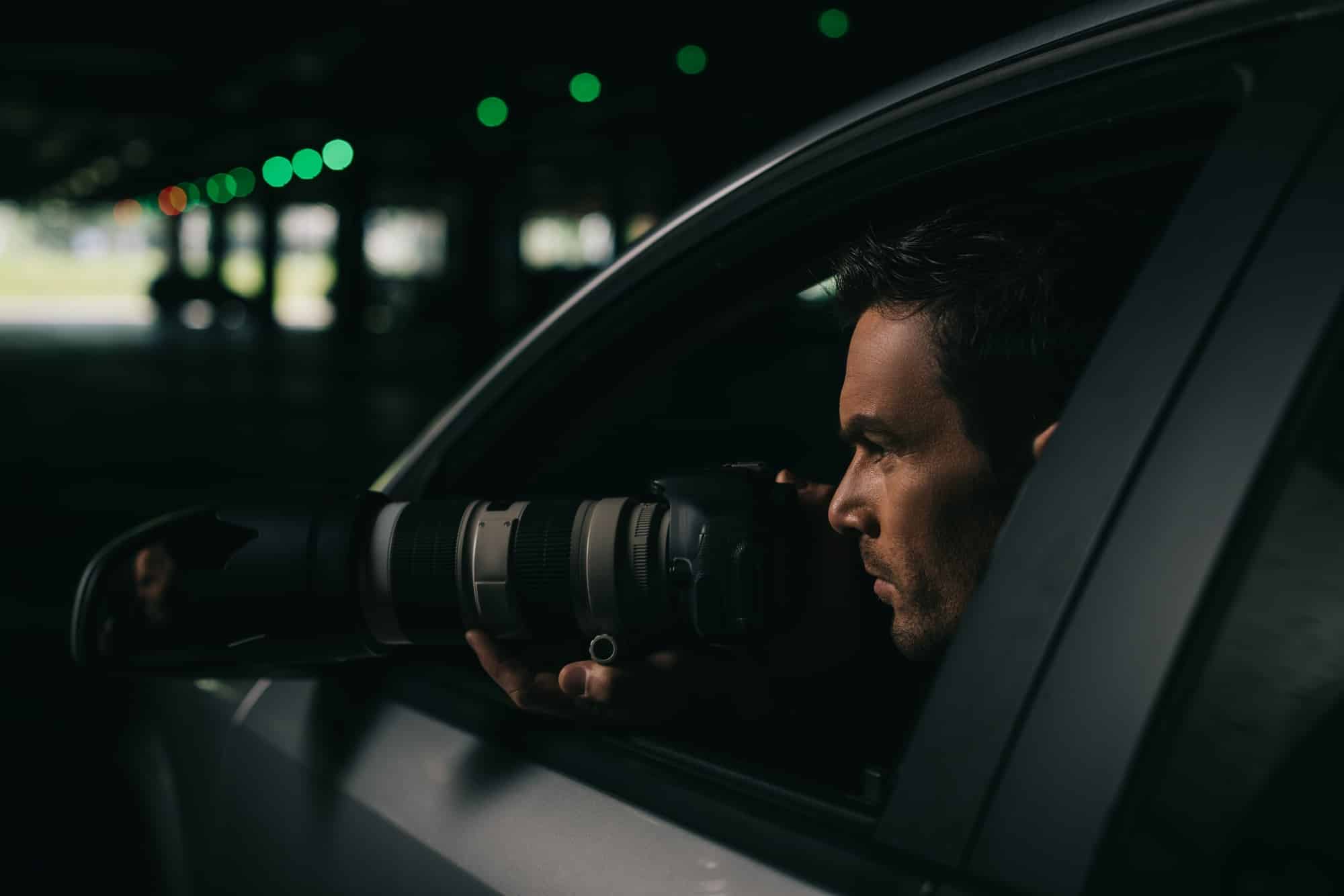 side view of male paparazzi doing surveillance with camera from his car detective privé